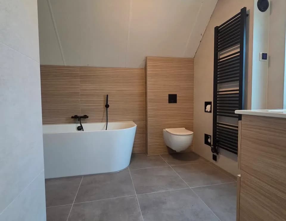 Afgewerkte badkamer met houtlook wand, ligbad en toilet